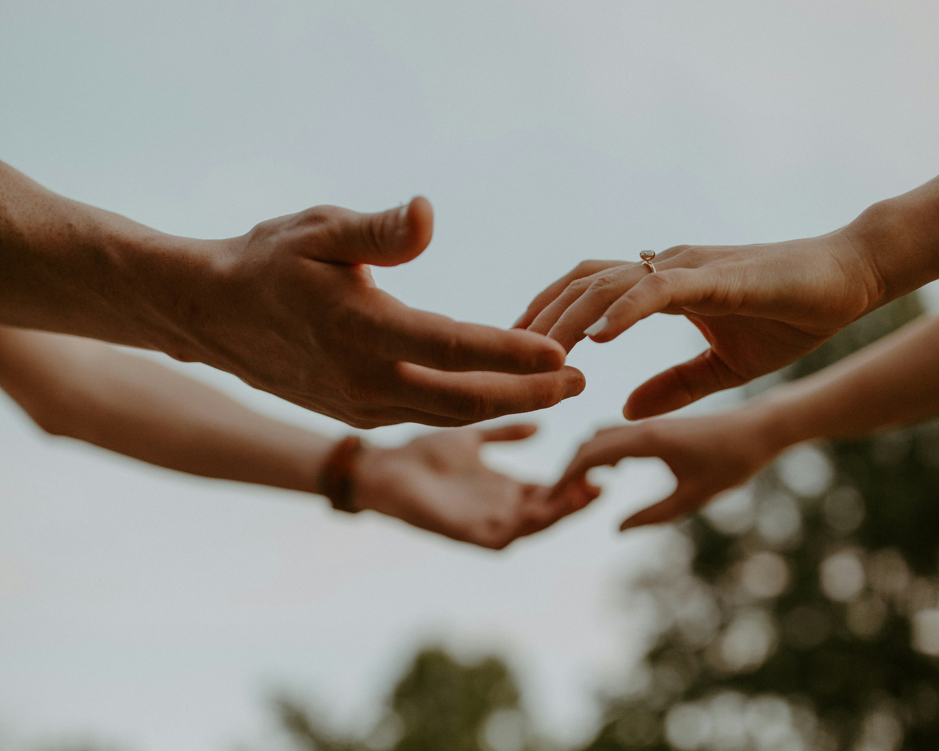 Two pairs of hands meeting in soft light, one offering a ring to the other.